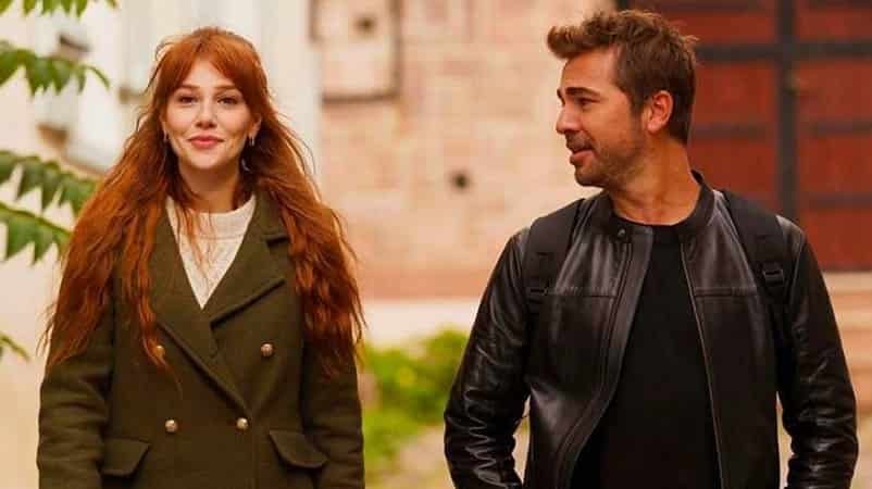 leading actors of the turkish romantic drama series Çöp Adam , Elçin Sangu smiling walking down the street, wearing a green coat with a white blouse and red long hair, next to Engin Altan Düzyatan looking at her and wearing a black leather jacket with a t-shirt of the same color
