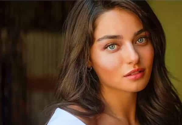 Ayça Ayșin with brown hair and blue eyes, wearing a white blouse