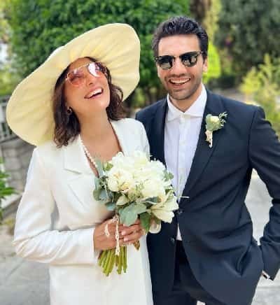 Kaan Urgancıoğlu wearing a groom suit next to his girlfriend now wife and bride Burcu Denizer wearing a big hat a white suit with a white rose bouquet, their wedding took place in athens